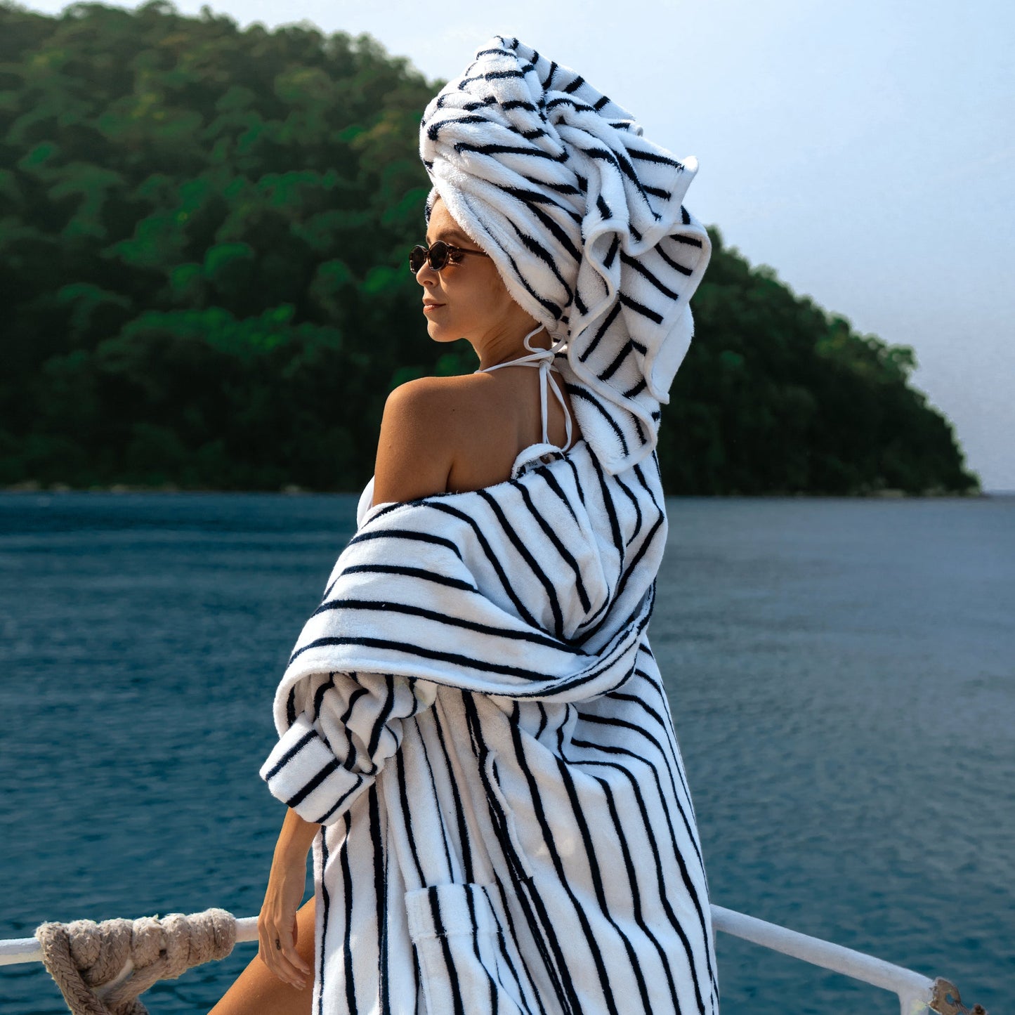 Woman wrapped in a black and white striped towel on a boat with a scenic background