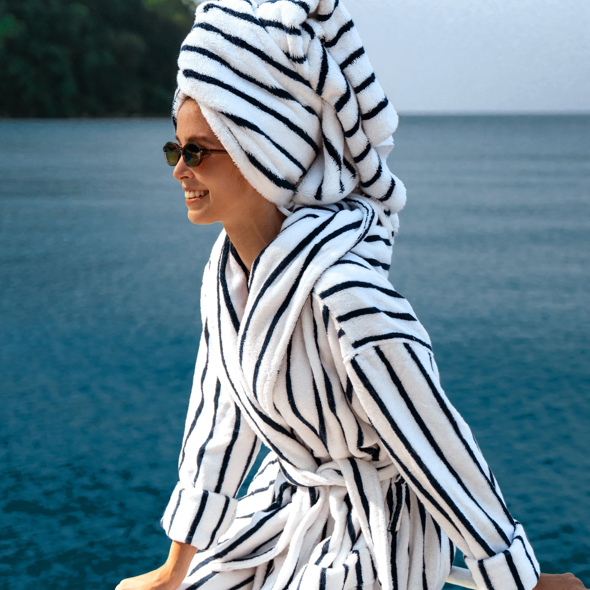 Person wearing a black and white striped robe and towel by a body of water