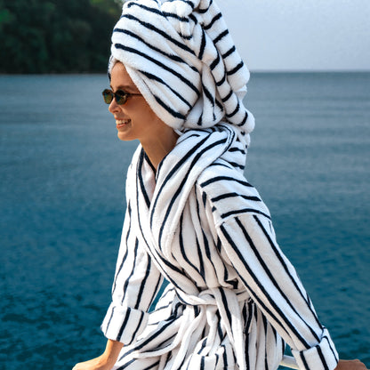 Person wearing a black and white striped robe and towel by a body of water