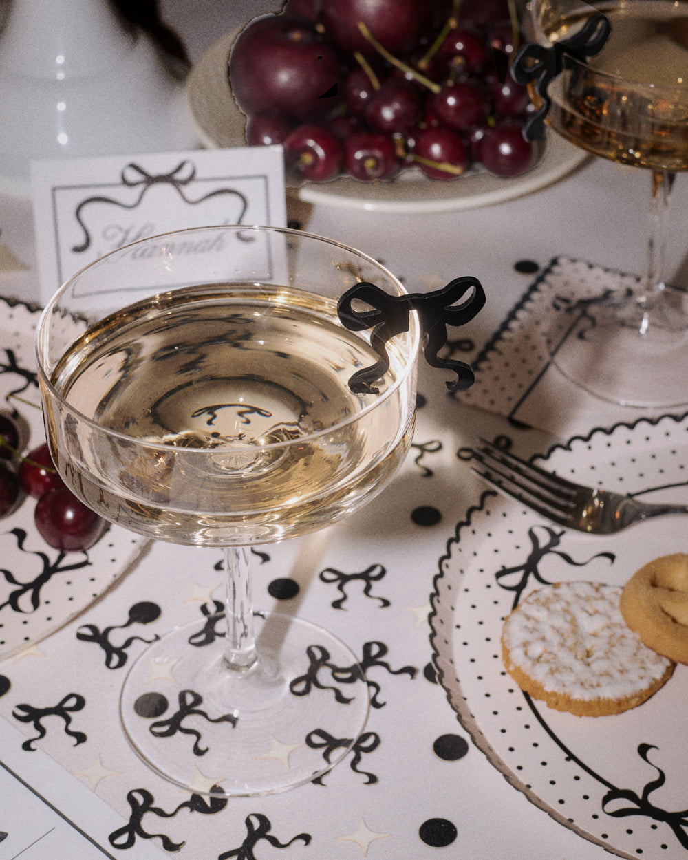 Glass of white wine on a decorative tablecloth with grapes and cookies.