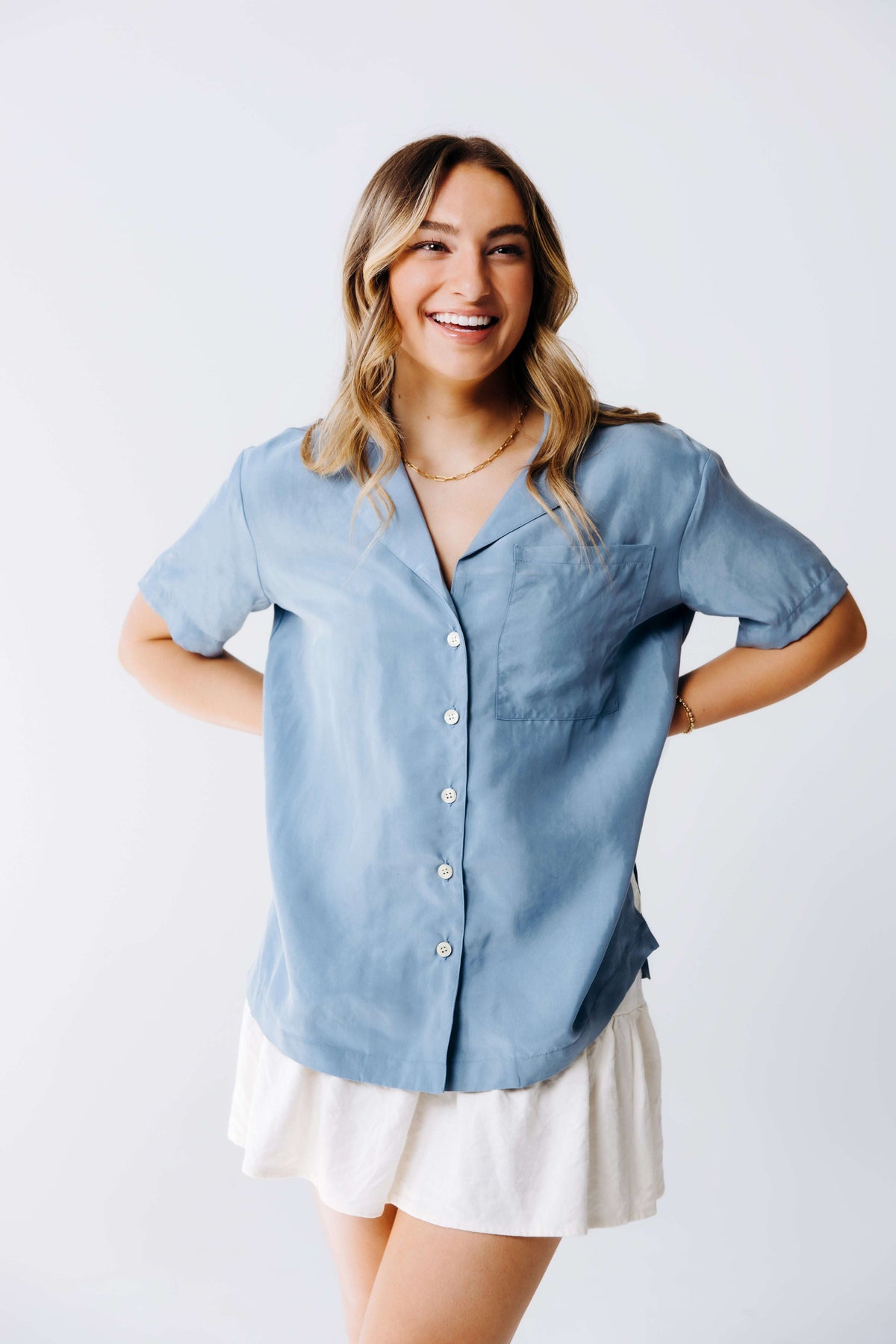 Woman wearing a light blue button-up shirt and white skirt on a plain background