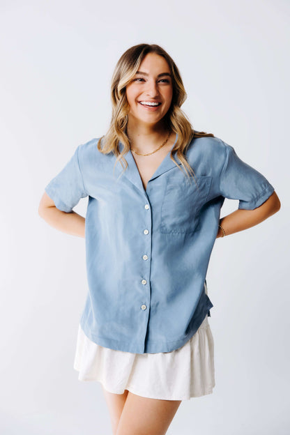 Woman wearing a light blue button-up shirt and white skirt on a plain background
