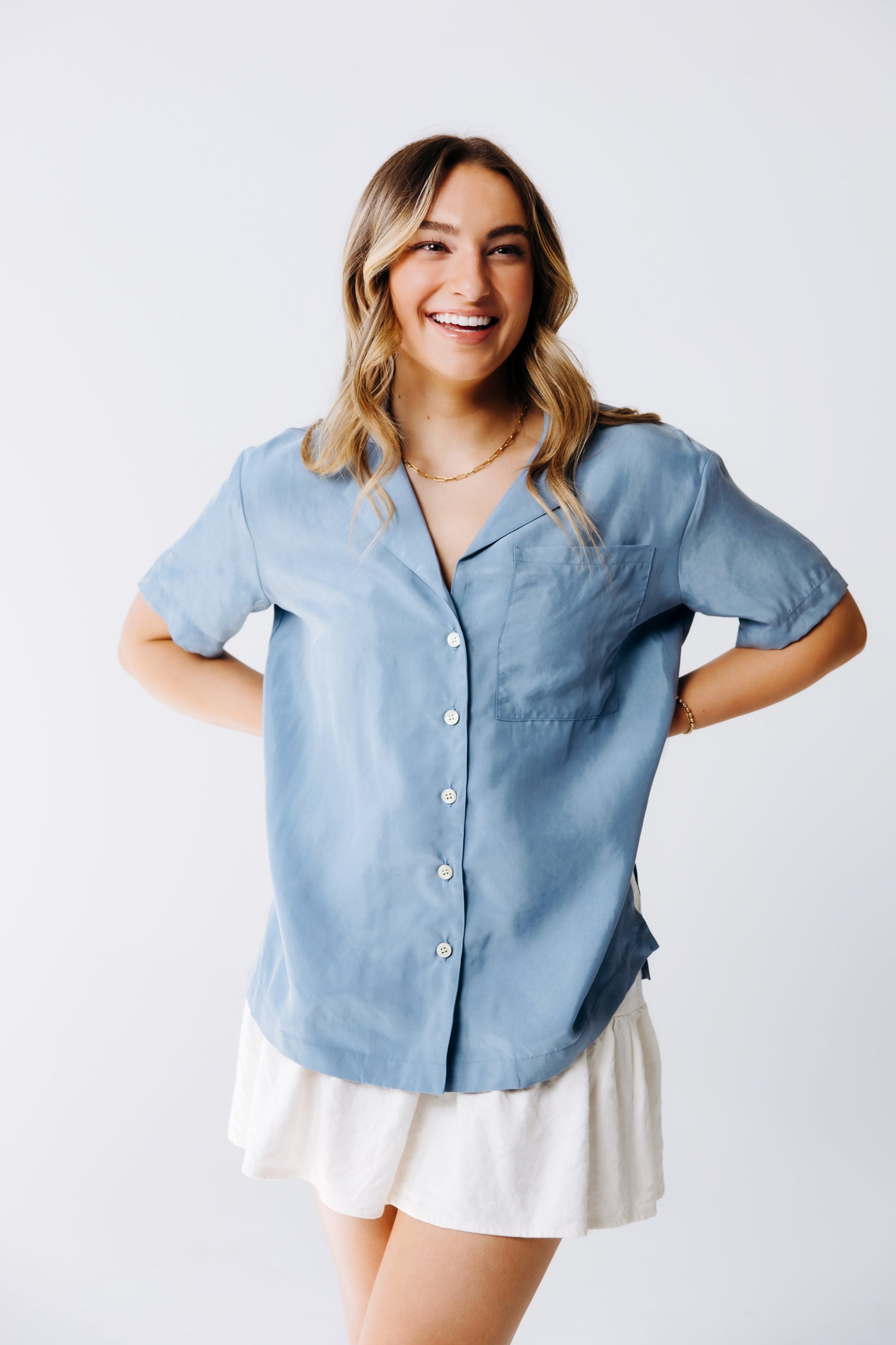 Woman wearing a light blue button-up shirt and white skirt on a plain background