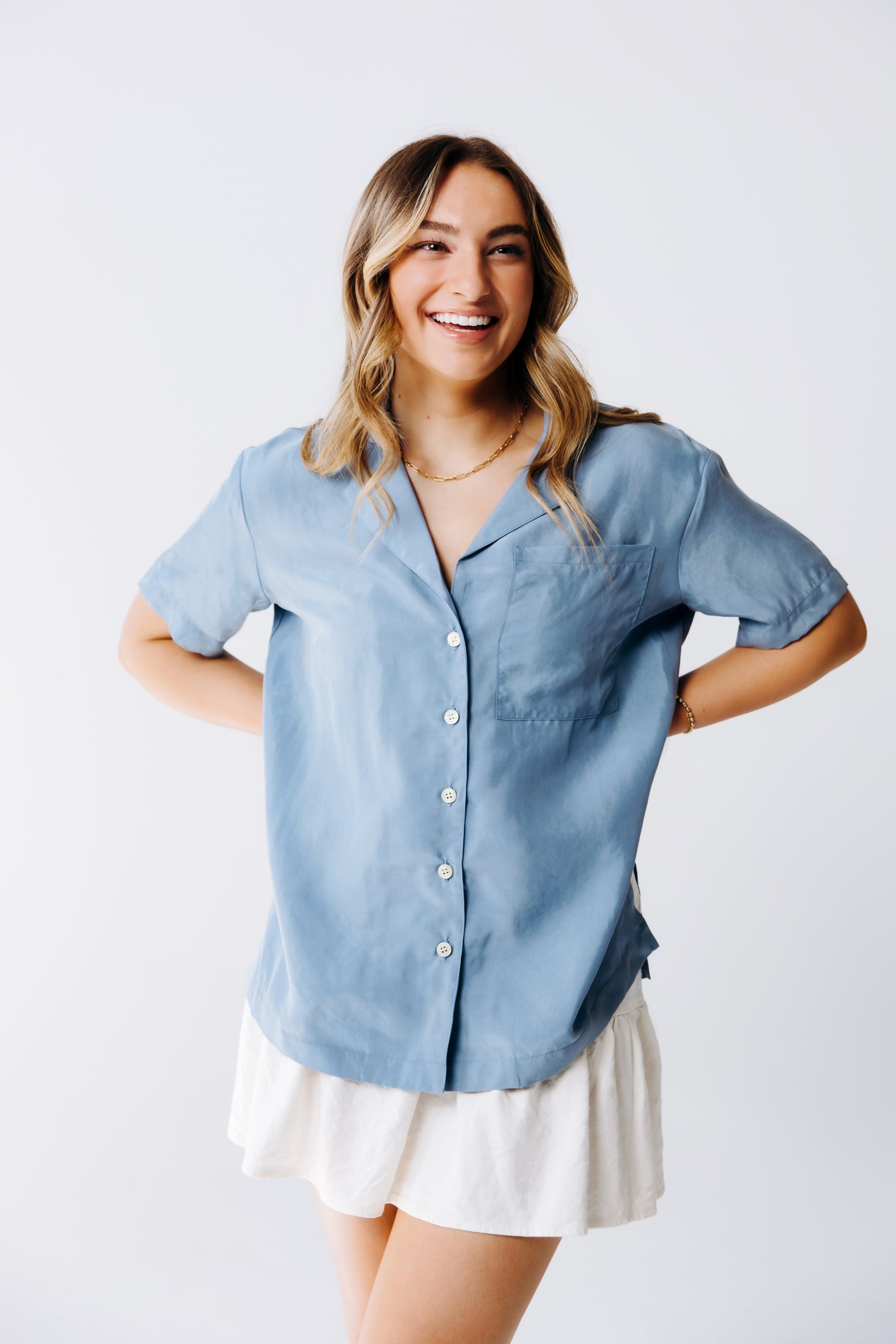 Woman wearing a light blue button-up shirt and white skirt on a plain background