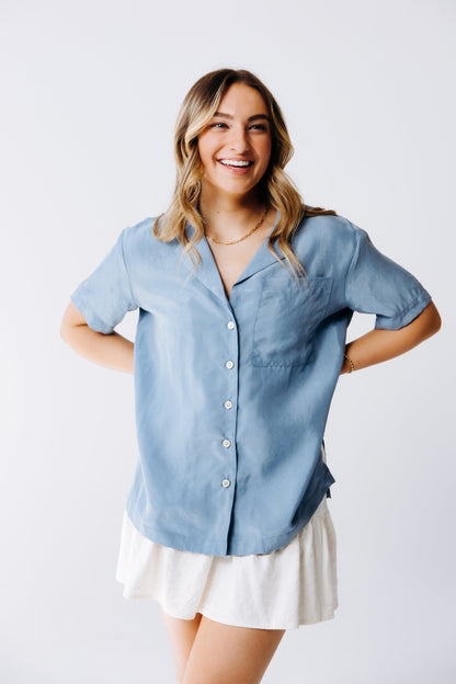 Woman wearing a light blue button-up shirt and white skirt on a plain background