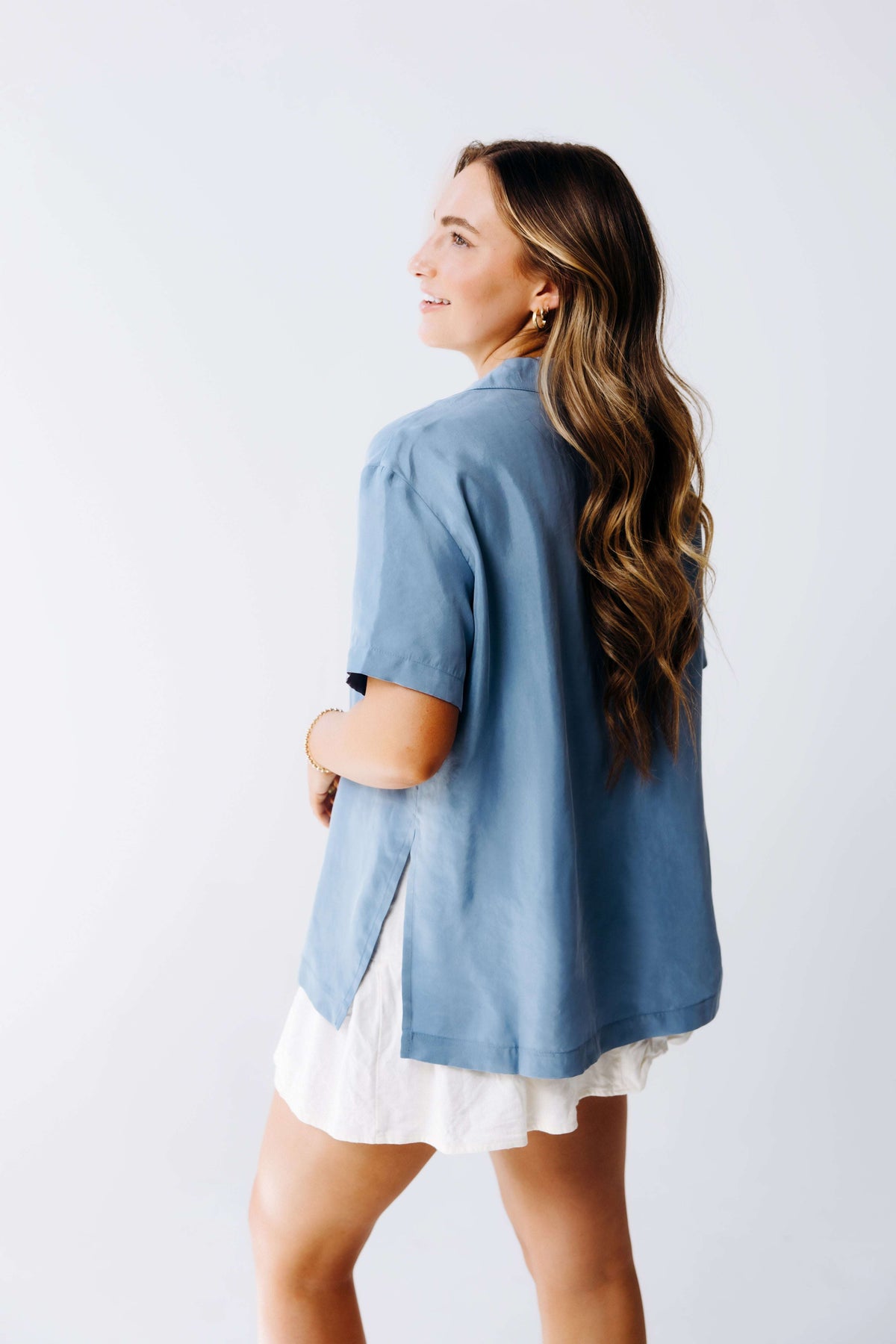 Woman wearing a blue shirt over a white dress against a plain background