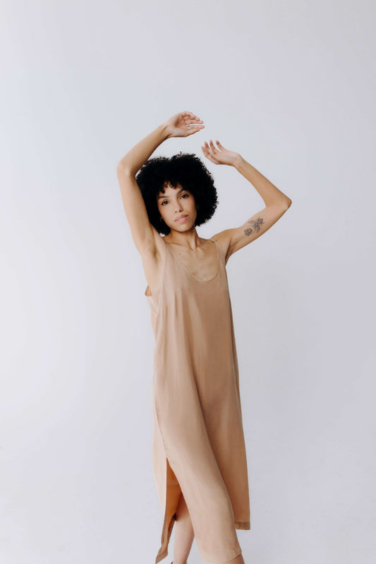 Woman wearing a beige dress with arms raised against a plain background