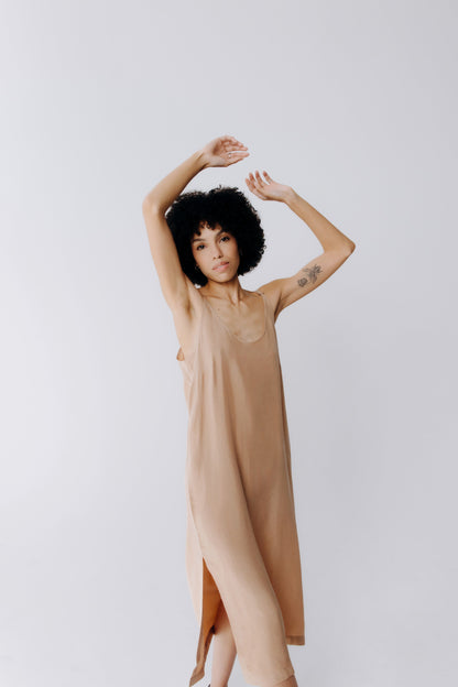 Woman wearing a beige dress with arms raised against a plain background