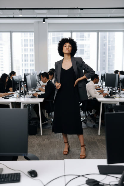 Woman wearing a black slip dress in an office with a jacket over the dress.