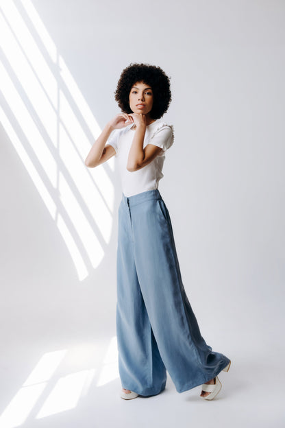 Woman wearing a white top and light blue wide-leg pants against a white background