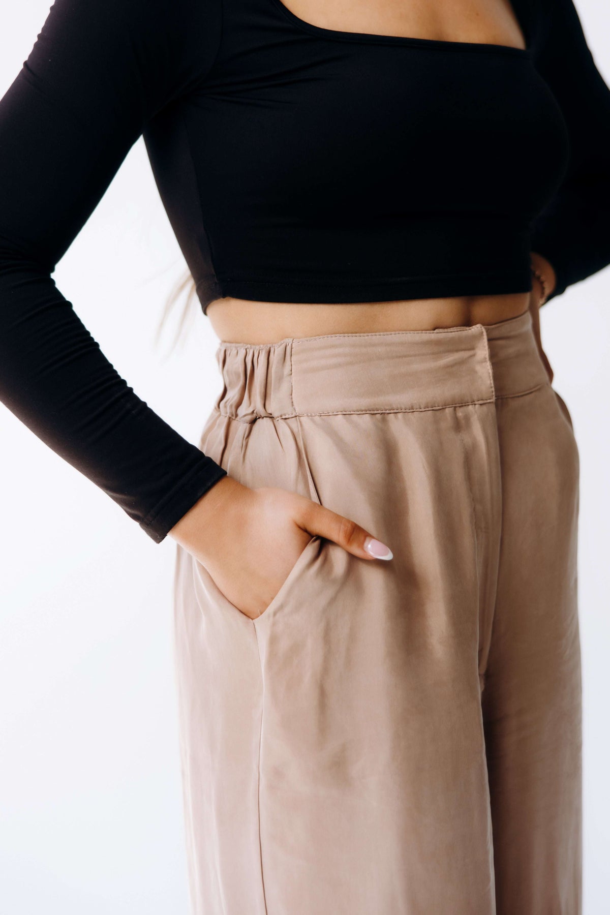 Person wearing a black long-sleeve top and beige pants on a white background