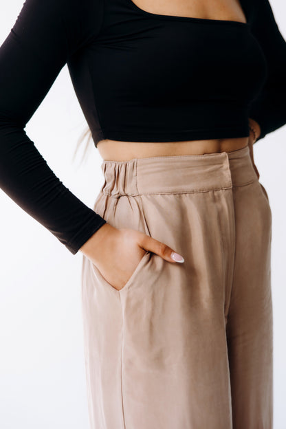 Person wearing a black long-sleeve top and beige pants on a white background