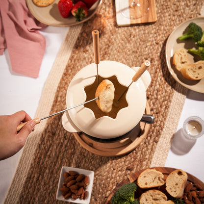 Fondue pot with bread being dipped into a melted cheese fondue on a table with various food items.