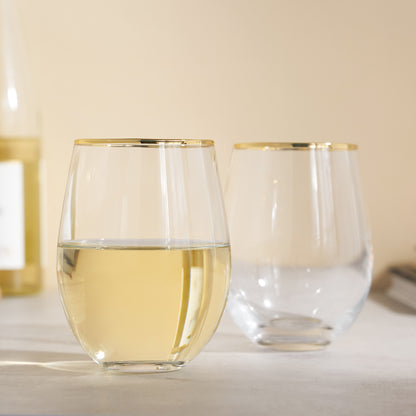 Two clear stemless wine glasses with gold rims on a light surface.