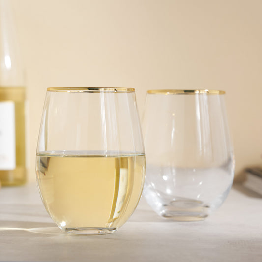 Two clear stemless wine glasses with gold rims on a light surface.