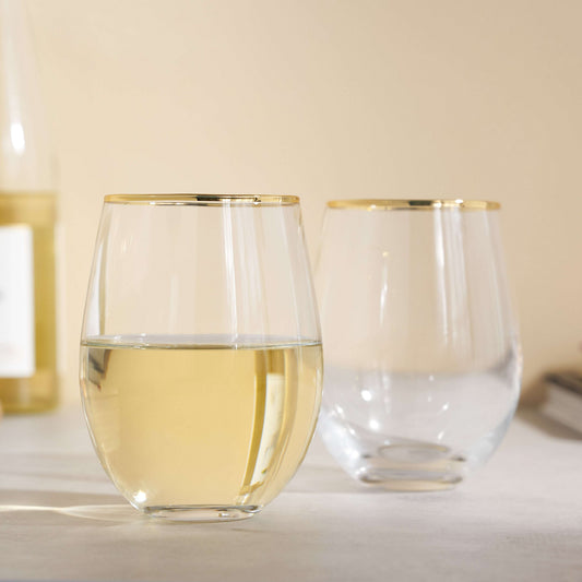 Two clear stemless wine glasses with gold rims on a light surface.